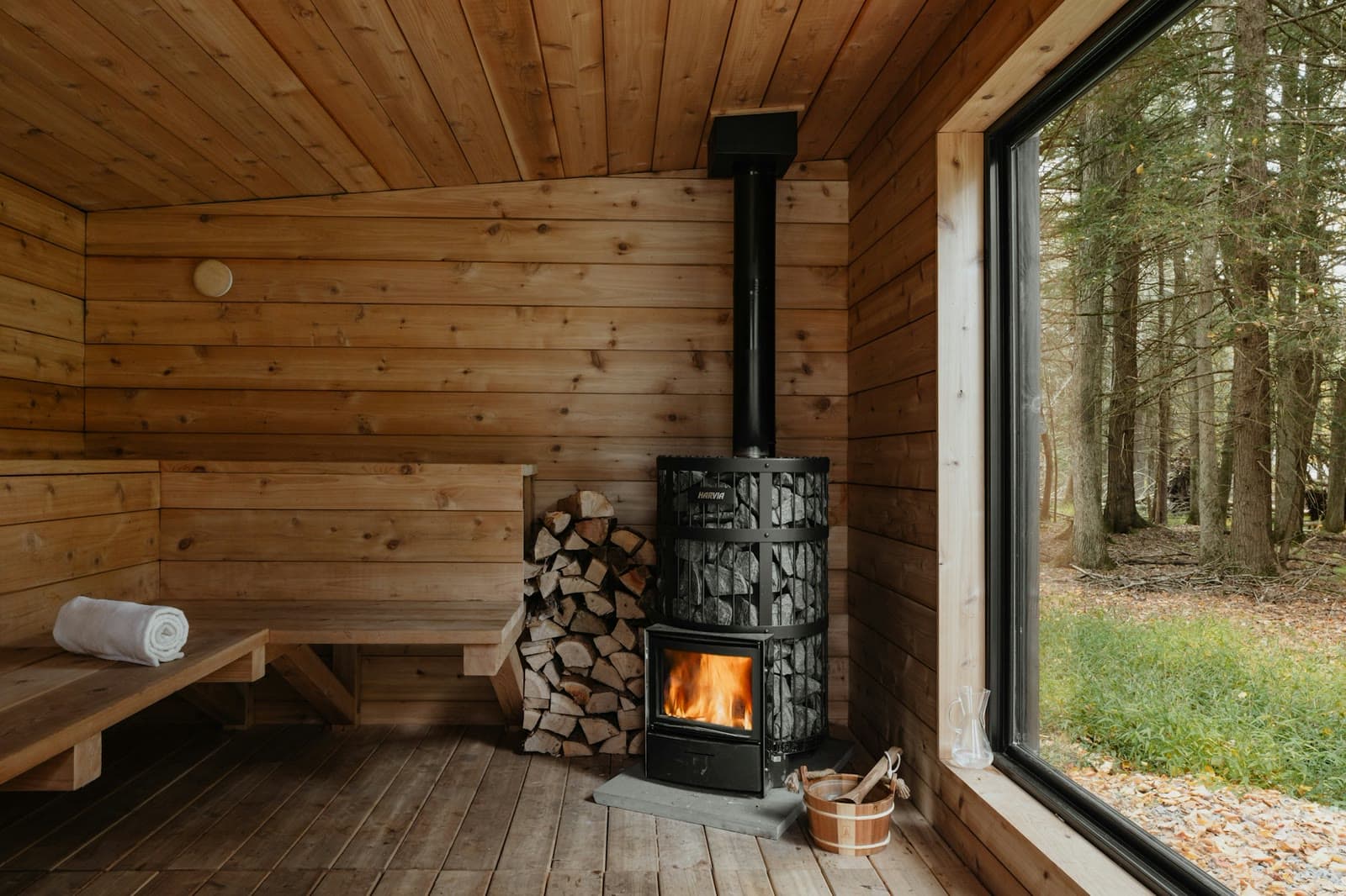 A timber sauna with a wood-burning stove and a forest view